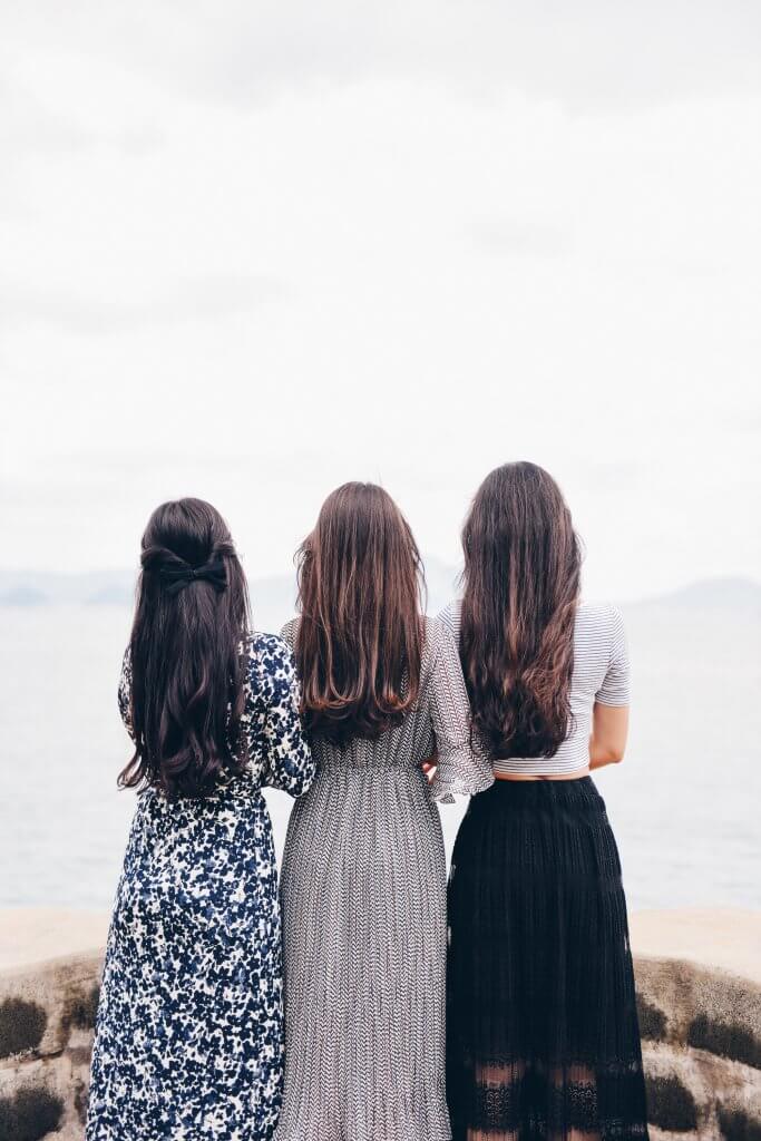 3 brunette girls with long hair overlooking an ocean wearing dresses