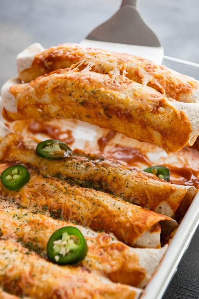 9x13 pan with enchiladas and two enchiladas being taken out of the pan with a spatula