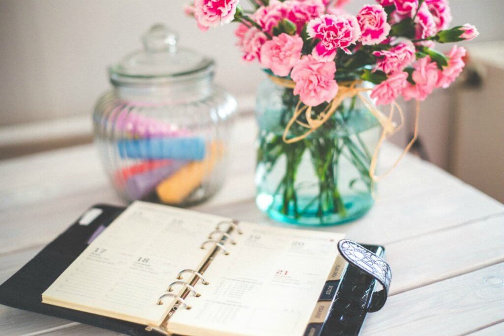 A planner, flowers and bowl on a white table