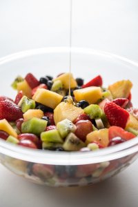 bowl of fruit salad with honey being drizzled on top of it