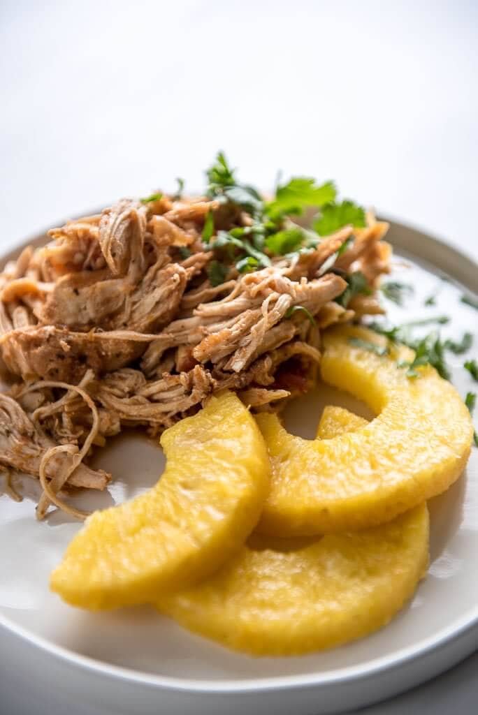 Slow Cooker Salsa Chicken on a white plate garnished with pineapple slices and cilantro