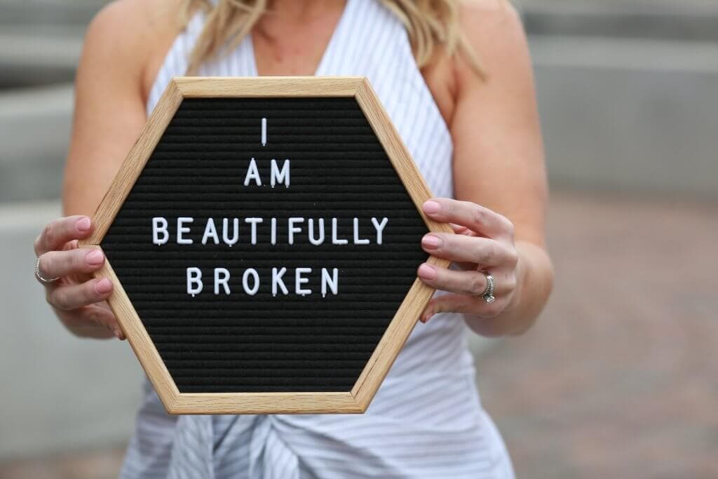 A woman holding a sign that says I am Beautifully Broken