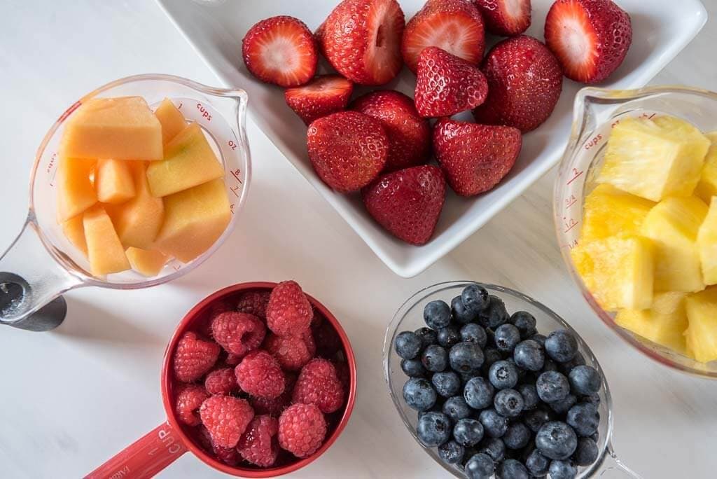 Dishes filled with Cantaloupe, strawberries, raspberries, blueberries, pineapple 