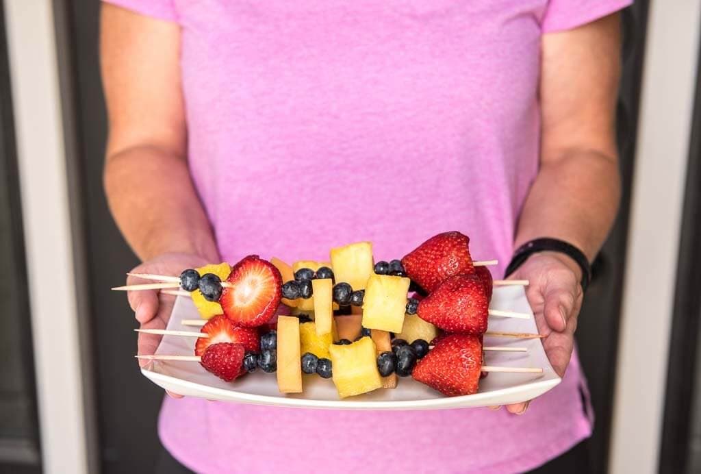 A woman holding a plate of fruit kabobs
