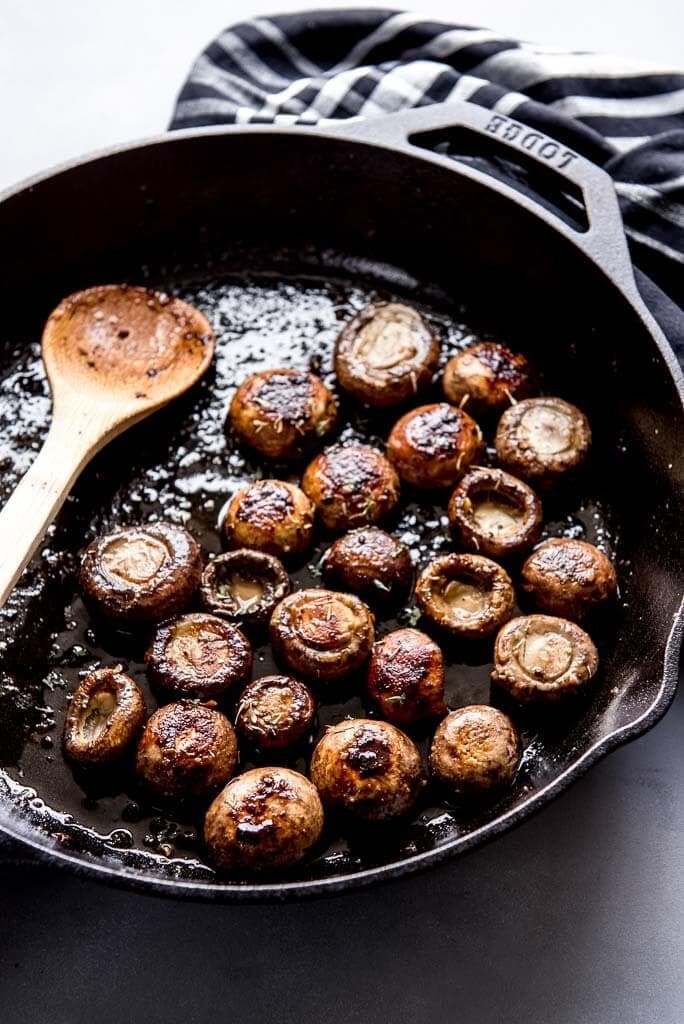 Cast iron skillet with sautéed mushrooms and a wooden spoon and napkin