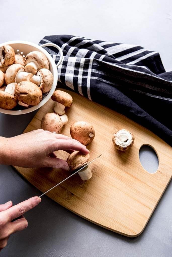 Woman cutting stems off mushrooms on a wooden cutting board with a napkin
