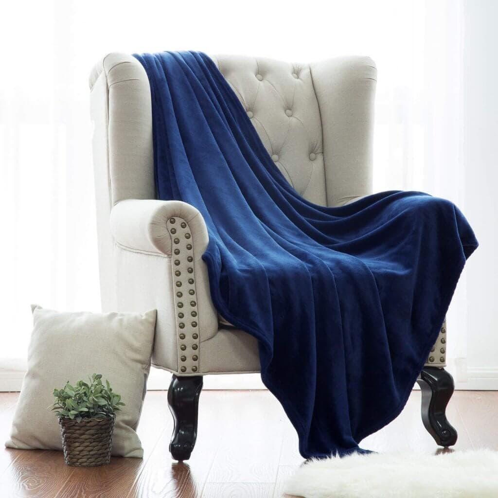 A white chair with a pillow and plant on the floor and a blue blanket draped over the chair