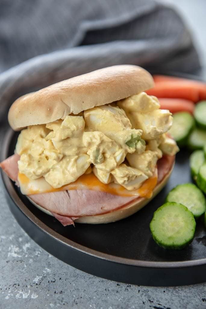 Air Fryer Ham and Cheese with Egg Salad on a bagel on a black plate with vegetables