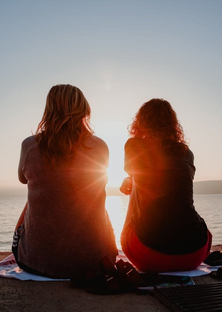 Two women sitting down facing the sun