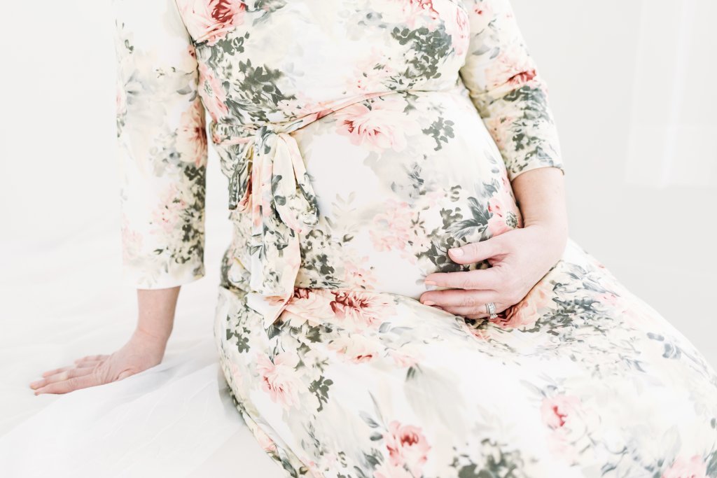 A pregnant woman in a floral dress holding her belly