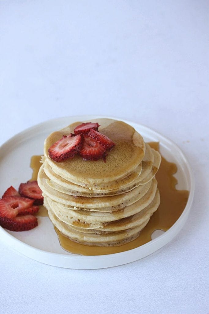 A stack of gluten free pancakes with strawberries and syrup on top