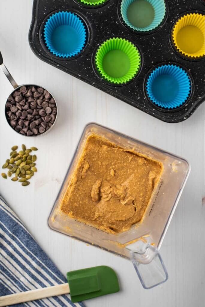 pumpkin muffin batter in a blender with chocolate chips and pumpkin seeds with a muffin tin ready and lined