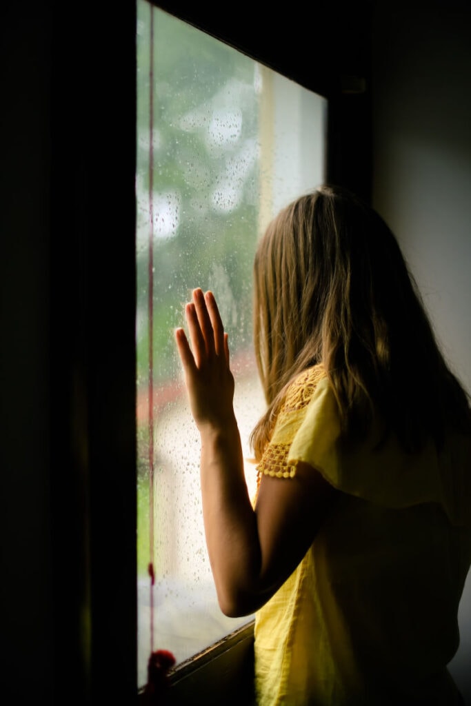 a woman looking out a window with her hand on the glass