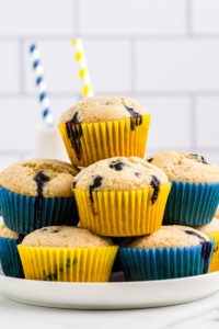 A stack of lemon blueberry muffins with yellow and blue liners on a white plate