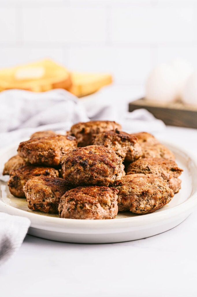 a pile of homemade breakfast sausage patties on a white plate with a cloth white napkin
