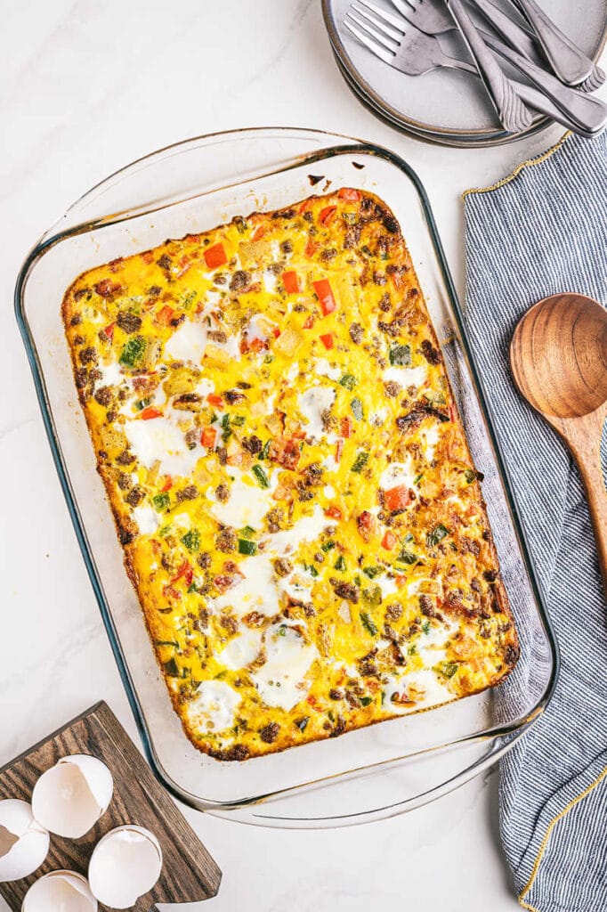 a 9x13 pan filled with breakfast casserole with eggs and a wooden spoon and grey napkin