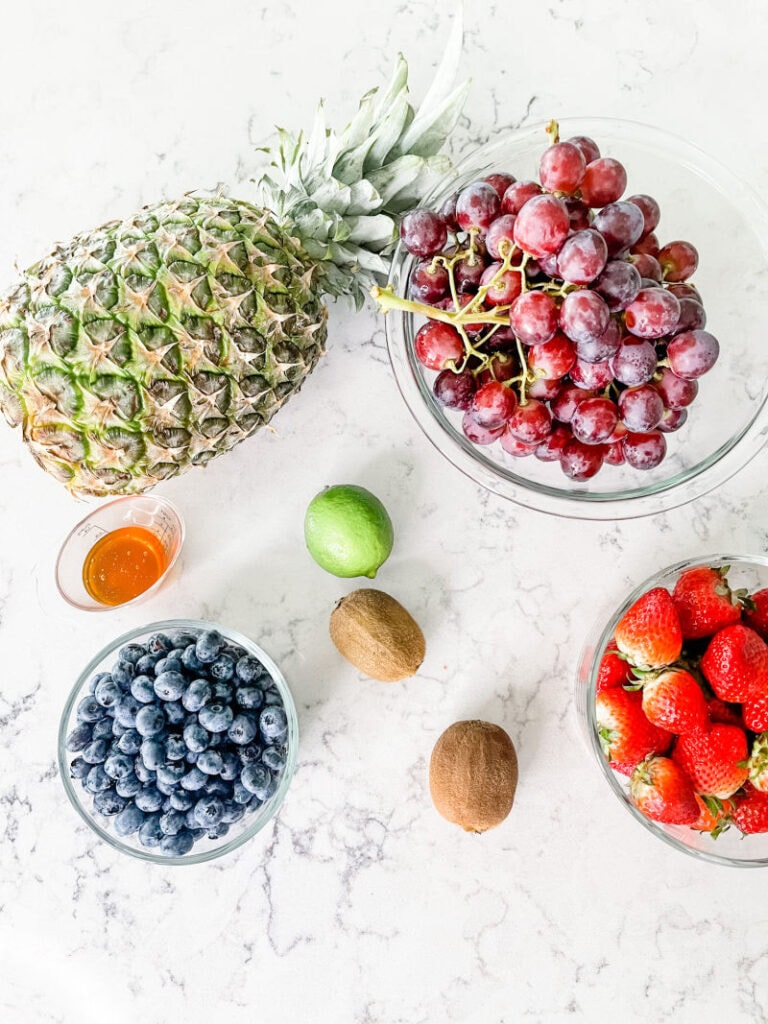 pineapple, honey, blueberries, kiwi, lime, strawberries and grapes on a marble counter