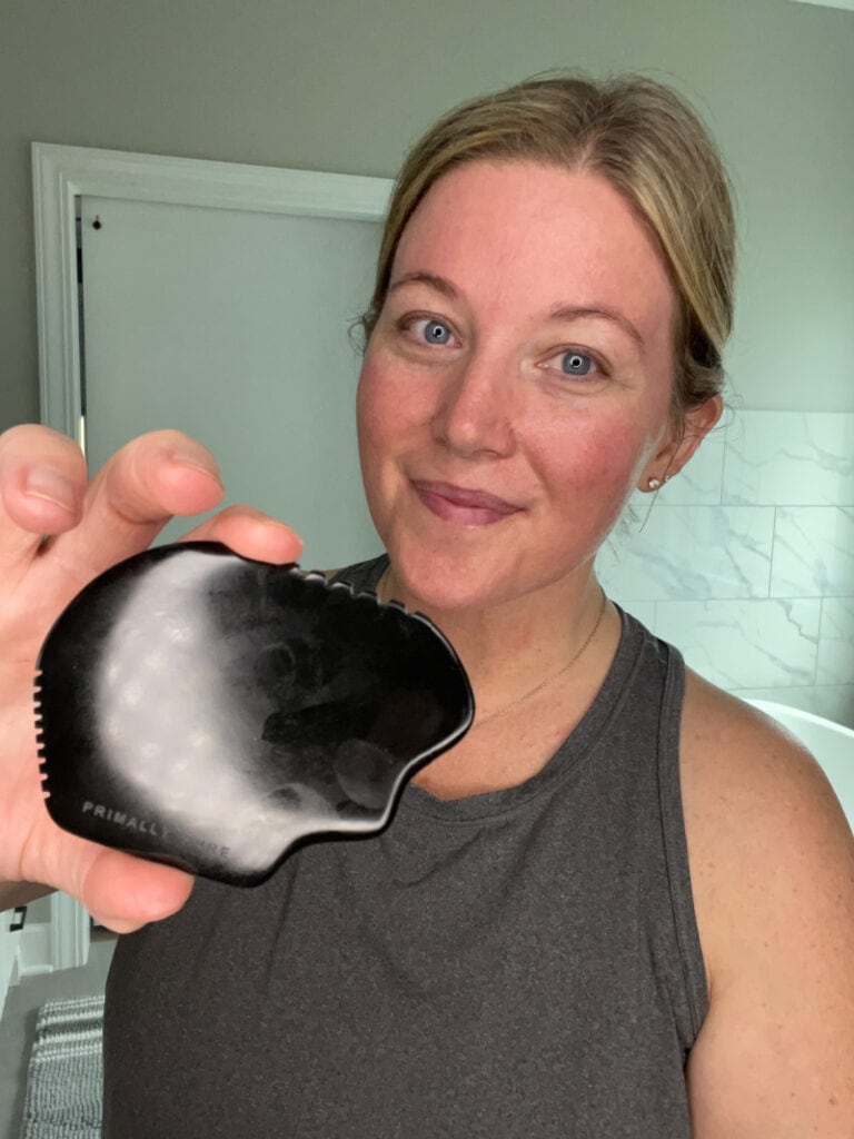 a woman smiling and holding a black gua sha stone