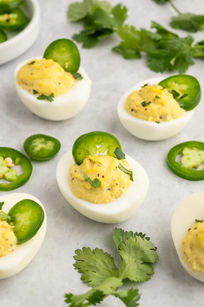 a white plate covered with deviled eggs with jalapenoes on top and cilantro