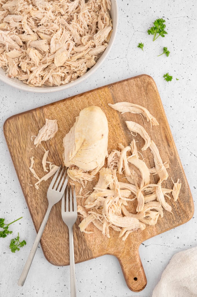 cooked chicken on a wooden cutting board with 2 forks to shred the chicken