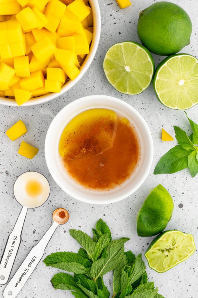 tangy dressing in a white blowl with sliced limes and mangoes in a bowl with mint and basil