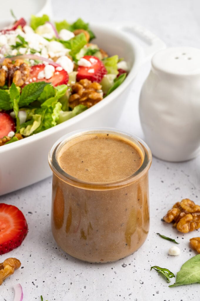 a cup of creamy balsamic dressing with strawberry goat cheese salad behind it